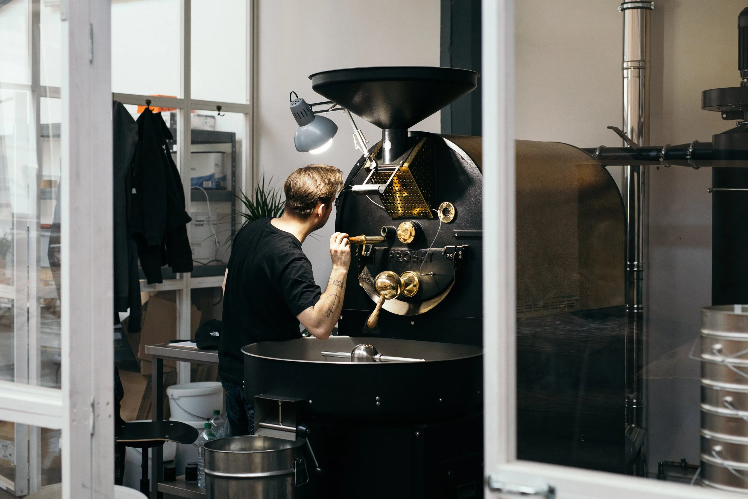 Coffee roaster operating a large black roasting machine in a specialty roastery.