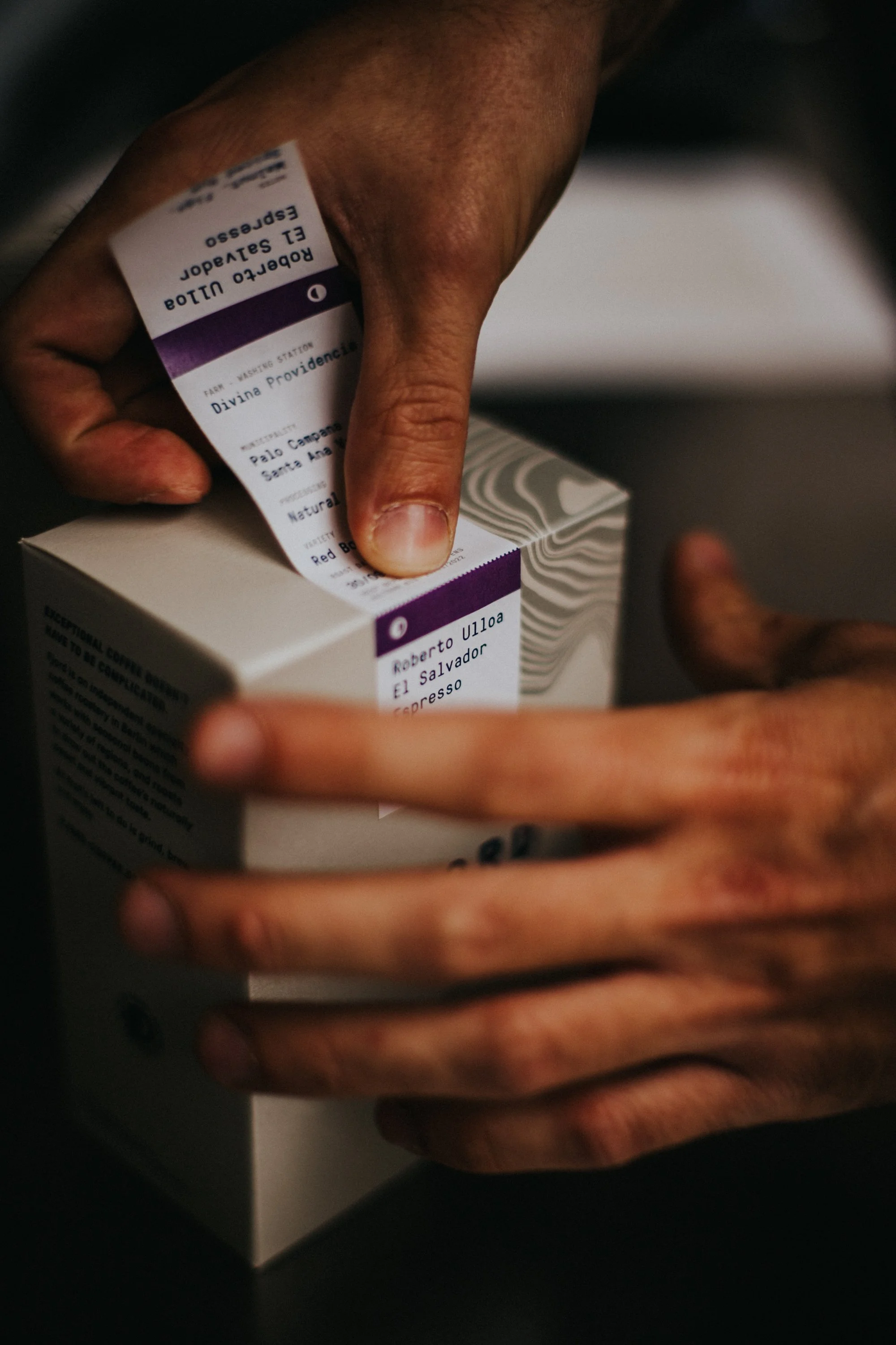 Close-up of hands opening a box of coffee capsules with a label indicating the flavor and origin.